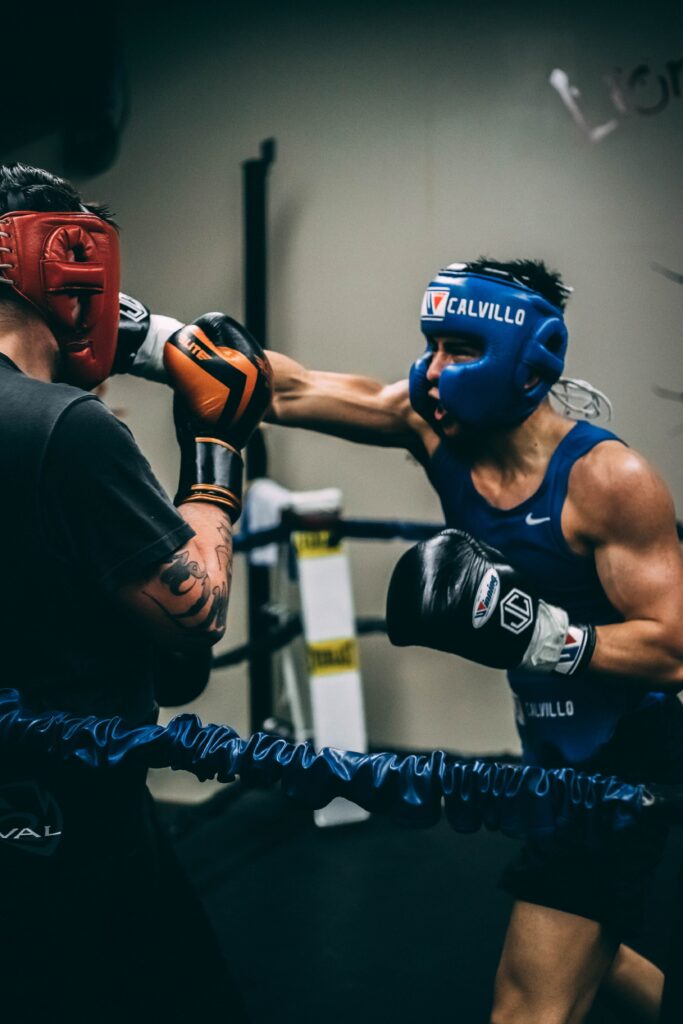 A photo of two male boxers in the ring, the boxer wearing blue is throwing a right hand punch at his opponent.