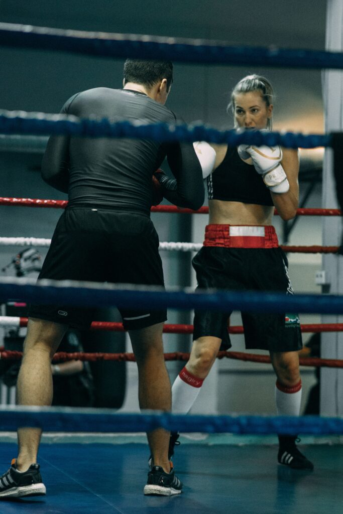 A photo taken through the ropes of a woman and a man training in the ring.