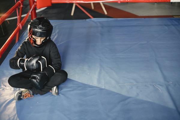 A child wearing a headguard and boxing gloves, sat in the boxing ring.